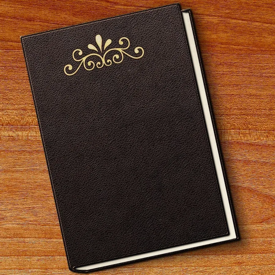 Um livro encadernado em pele preta com um ornamento dourado na capa lisa, numa mesa de madeira