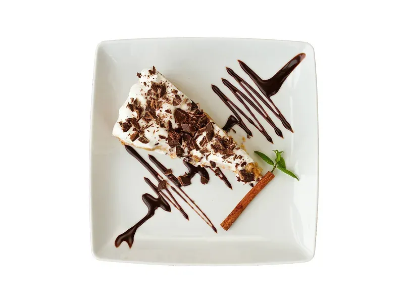 A slice of banoffee pie drizzled with chocolate on a square plate