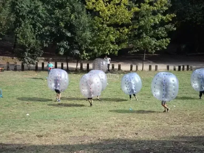 People inside inflatable bubbles playing football on a grass field
