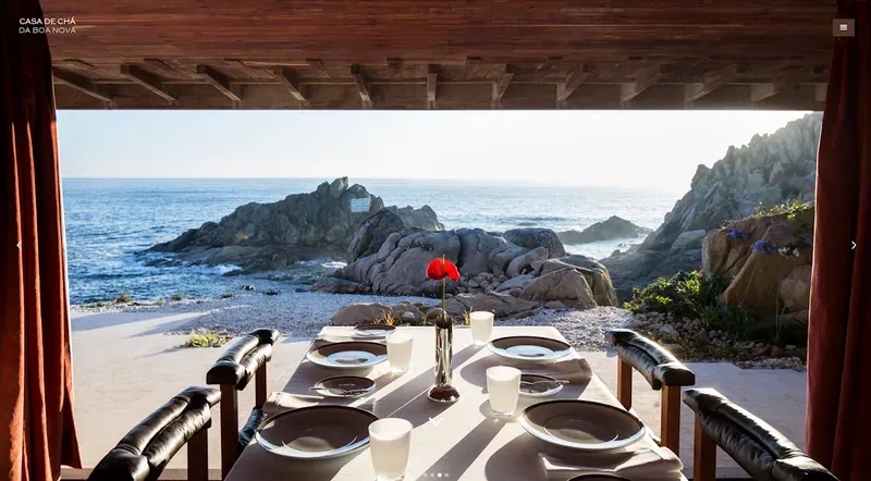 A set table looking out through a wide window onto rocks and the ocean
