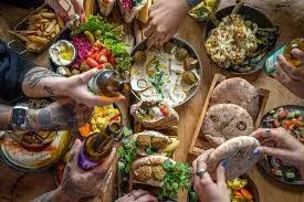 Hands reaching over a table full of pitas, salads and dips