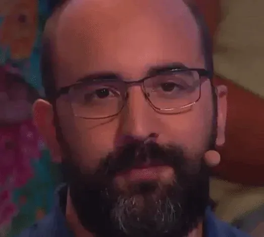 Animated GIF: a close-up of the same man, a small headset microphone at his cheek, staring into the camera with a deadpan look