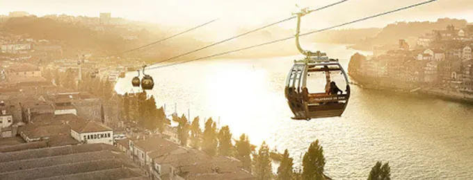 A cable car cabin gliding over riverside rooftops at sunset
