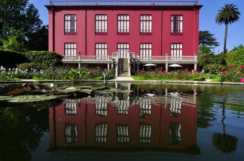 A red house reflected in a garden pond, surrounded by trees