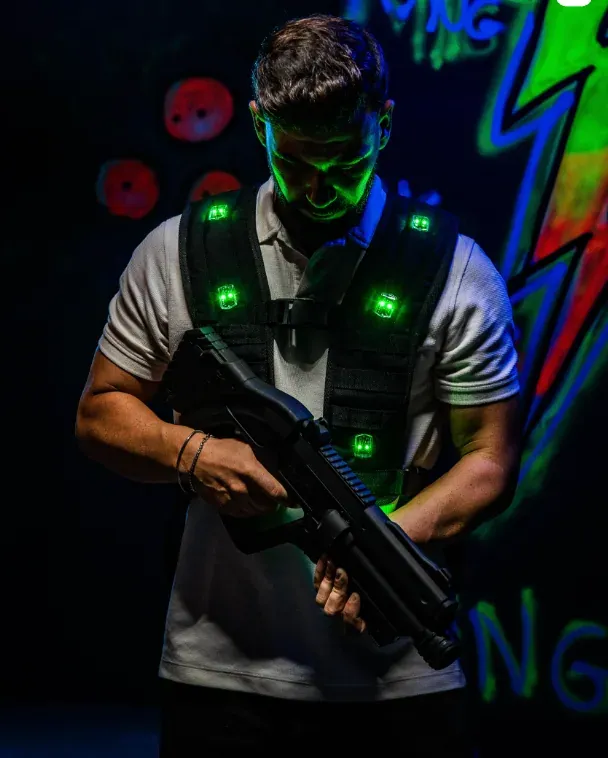 A player in a glowing vest aiming a laser tag gun in a dark neon arena