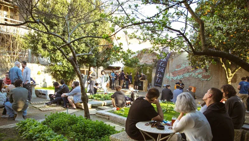 People drinking at tables in a sunny, tree-shaded beer garden