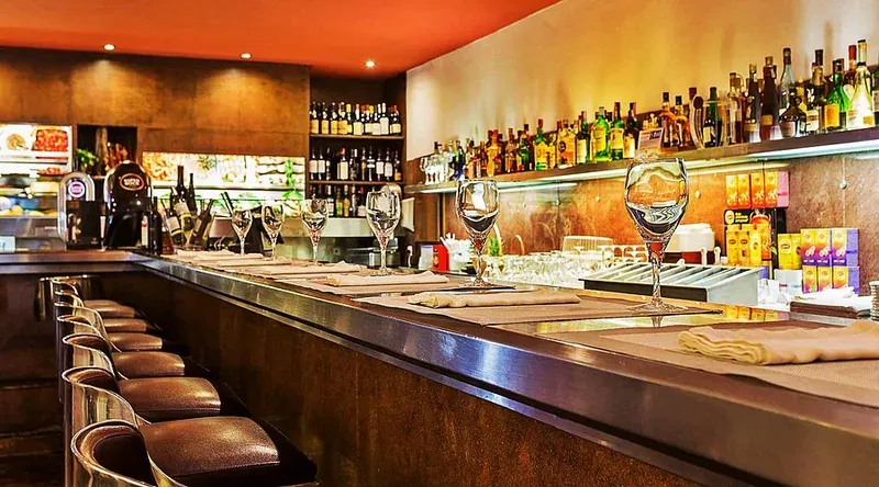 A long restaurant counter with bar stools and shelves of bottles