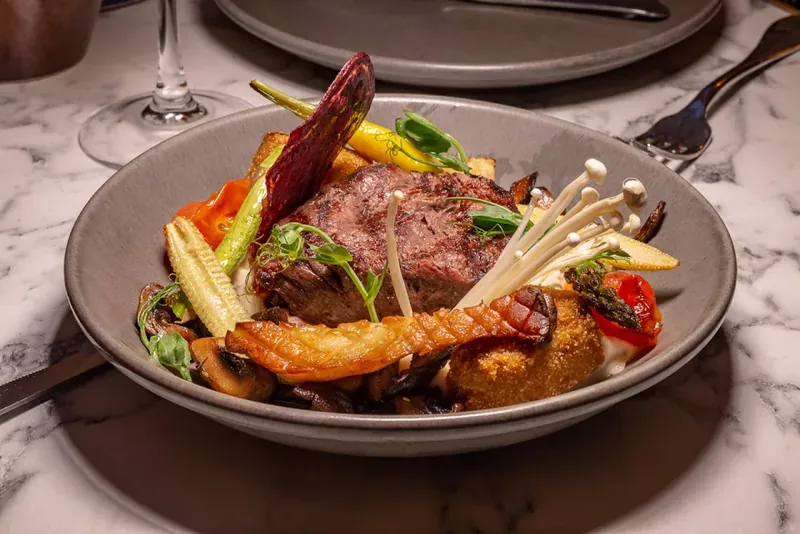 A plated dish of meat with grilled vegetables and mushrooms