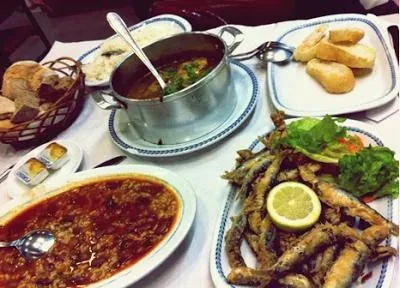 A table of Portuguese dishes: fried fish with lemon, a stew, bread and a pot of soup