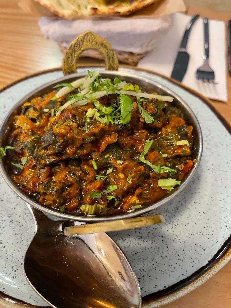 A curry in a copper serving bowl topped with fresh coriander