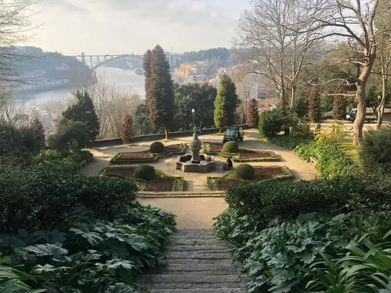 A formal garden with a fountain, with the river and a bridge beyond the trees