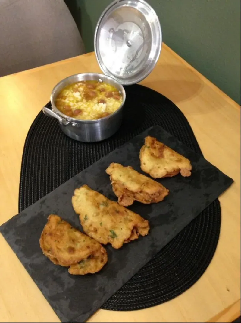 Fried pastries on a slate board next to a small pan of stew
