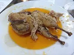 A whole roasted quail in an orange sauce on a white plate