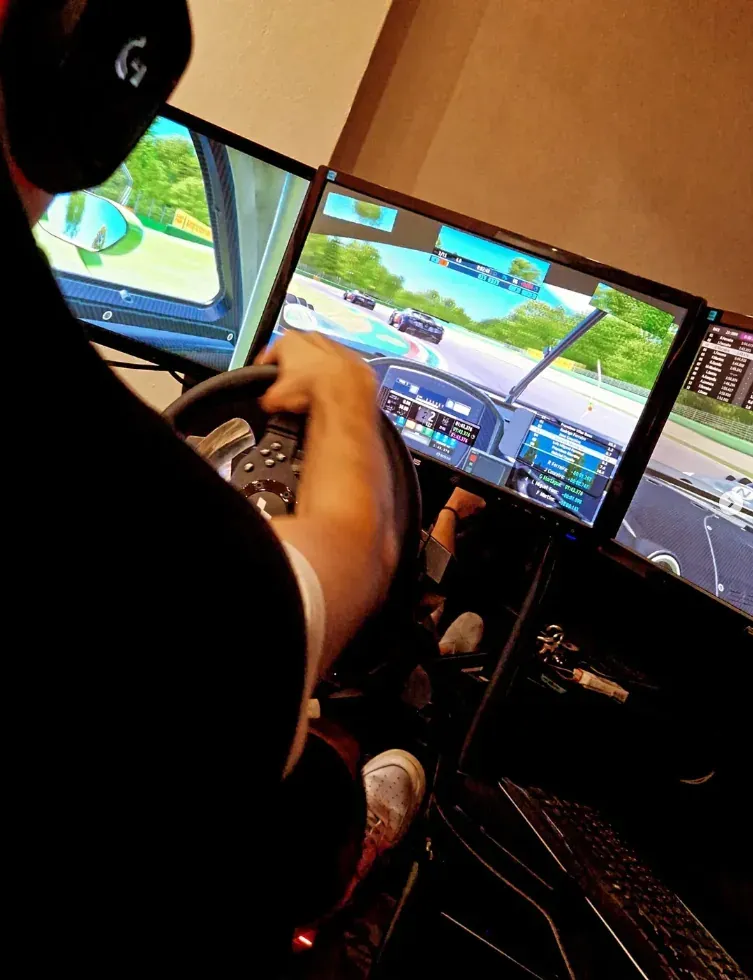 A driver in a racing simulator seat facing three screens