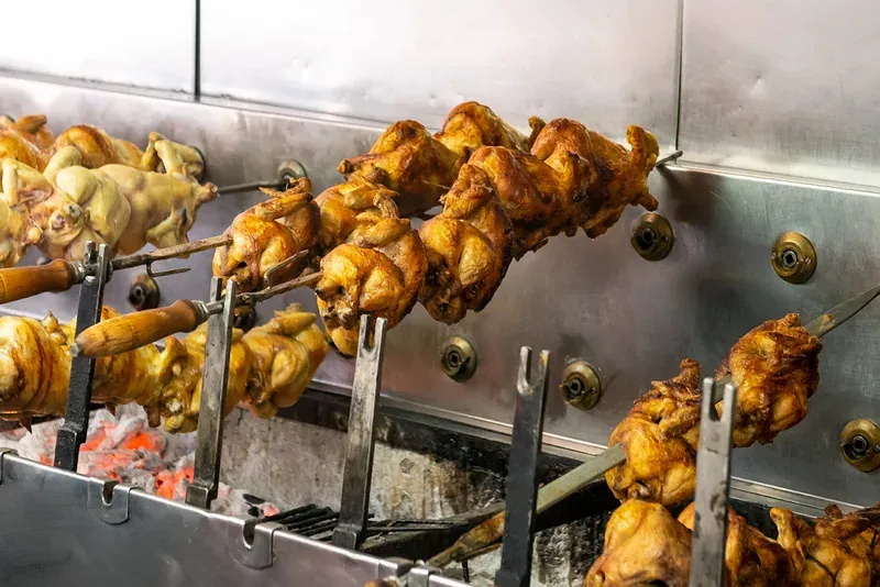 Rows of chickens roasting on spits over hot charcoal