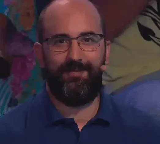 Animated GIF: a bearded man in glasses and a navy polo shirt smiles at the camera and slowly blinks