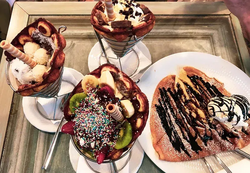 Ice-cream sundaes in tall glasses next to a crêpe with chocolate sauce