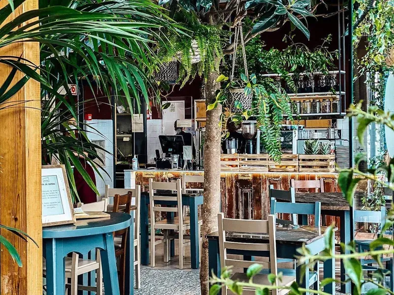 A leafy restaurant interior full of plants, with wooden tables and blue chairs