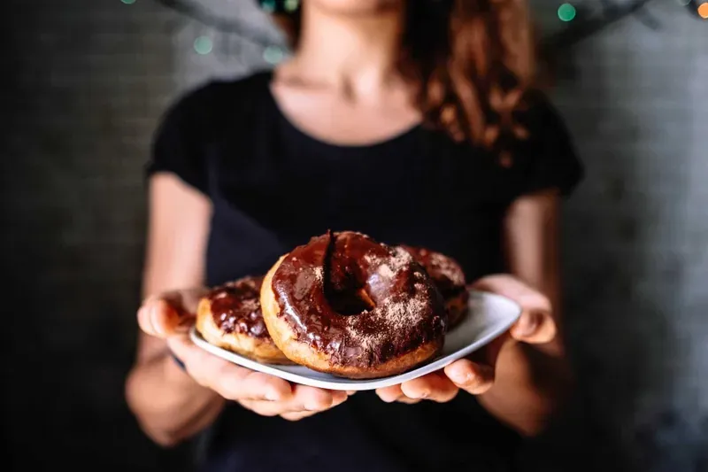 A person holding a plate with two chocolate-glazed donuts