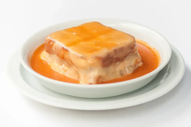 A vegan francesinha covered in melted cheese and orange sauce in a white bowl