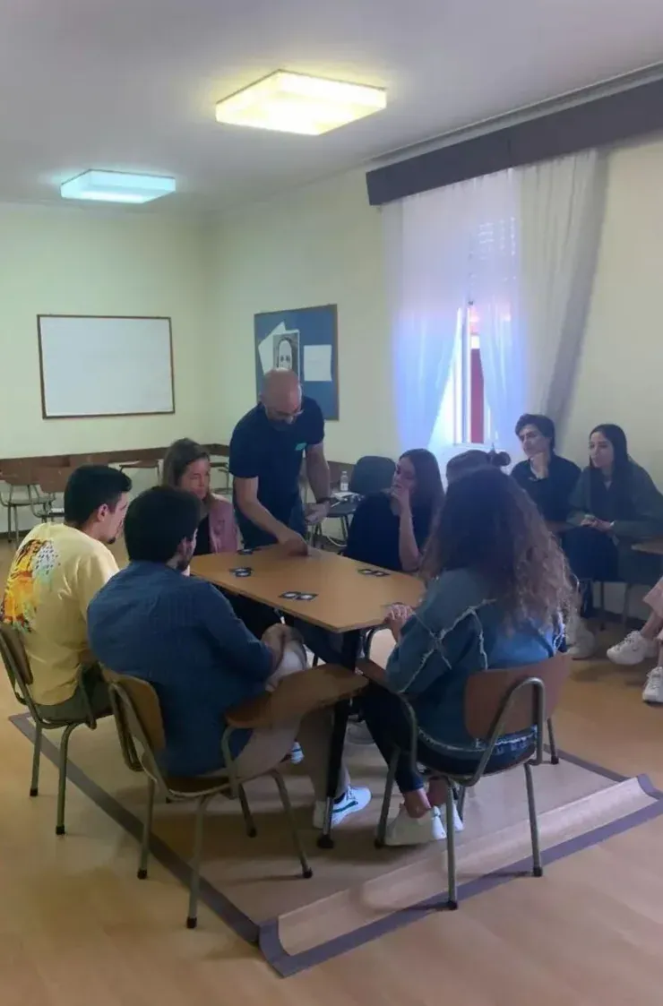 A facilitator lays cards on a table while a group of young people seated around it watch