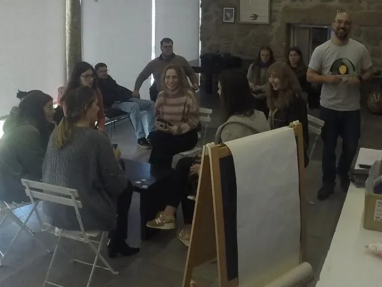 Participants sitting in a circle in a stone-walled room, laughing, while a standing facilitator talks