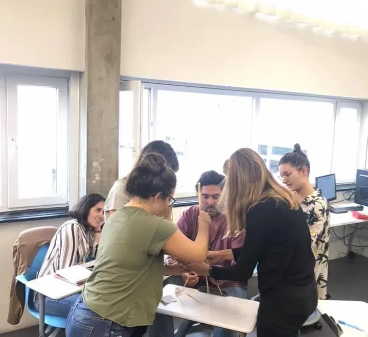 A group standing around a table, building a structure out of thin sticks together